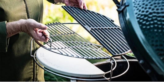 Een man is op de rand van een Big Green Egg een set-up aan het maken bestaande uit: een 1-piece conveggtor, een half conveggtor stone, een half cast iron grid en een half stainless steel grid.