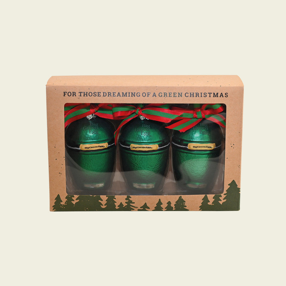 De set van 3 mini Big Green Egg kerstballen in hun verpakking. De verpakking is gemaakt van bruin karton en is voorzien van een doorzichtig kijkvenster. Boven het kijkvenster staat de tekst 'For those dreaming of a green christmas' en onder het venster zijn de silhouetten van groene kerstbomen gedrukt.