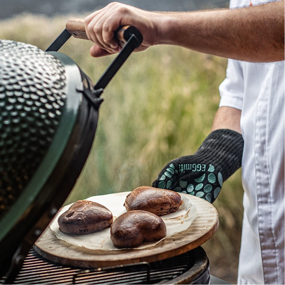 Dezelfde steen gelegen op een RVS rooster in een Big Green Egg. Op de baking stone ligt een rond stuk bakpapier met daarop 3 bruin gebakken, hartvormige koeken. 