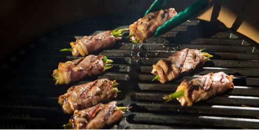 Close-up van het gietijzeren rooster in een Big Green Egg met opgerolde stukjes vlees met groente erin ,bakkend op de kamado.